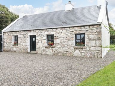 A stone cottage with three black windows and a black door surrounded by gravel at An Teach Ban in Rossaveel County Galway