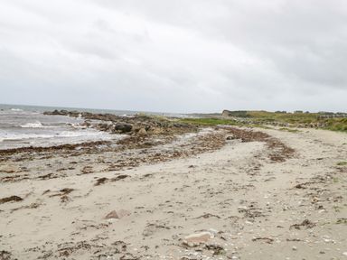 A sandy beach with rocks and seaweed along the shoreline at An Teach Ban in Rossaveel County Galway