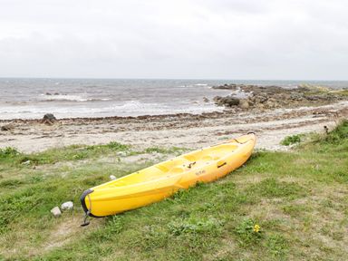 A yellow kayak on grass near a rocky beach and the ocean at An Teach Ban in Rossaveel County Galway