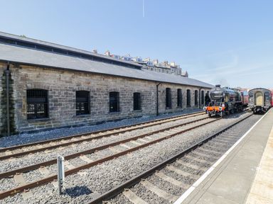 A railway station platform with tracks a stone building and a steam locomotive at Evening Star @ Engine Shed in Whitby