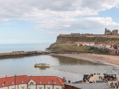 A coastal view with a yellow boat in harbor near houses and cliffs at Evening Star @ Engine Shed in Whitby