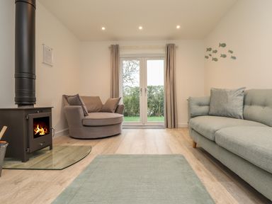 A living room with a wood stove a round armchair a sofa and glass doors with curtains at Kober House in Mullion