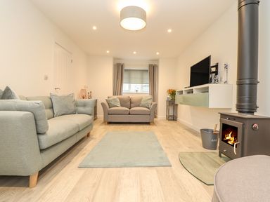 A living room with sofas a rug a wood burning stove and a wall mounted television at Kober House in Mullion