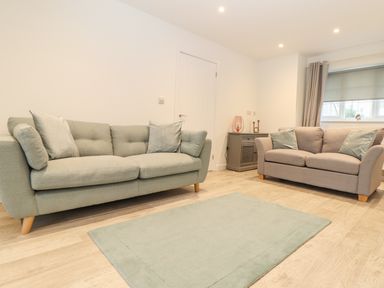 A living room with two sofas a small cabinet with decorations and a rug on the floor at Kober House in Mullion