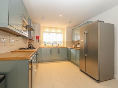 A kitchen with light green cabinets wooden countertops a large stainless steel refrigerator and a window at Kober House in Mullion