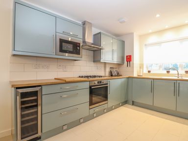 A kitchen with blue cabinets wooden countertops built in microwave oven stove and wine cooler at Kober House in Mullion
