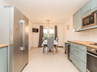 A kitchen with a stainless steel refrigerator a dining table with chairs and a microwave oven at Kober House in Mullion