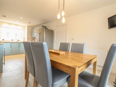 A dining area with a wooden table and gray chairs next to a kitchen with gray cabinets and a refrigerator at Kober House in Mullion