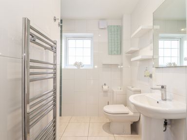 A bathroom with a toilet sink mirror towel rail and window at Kober House in Mullion