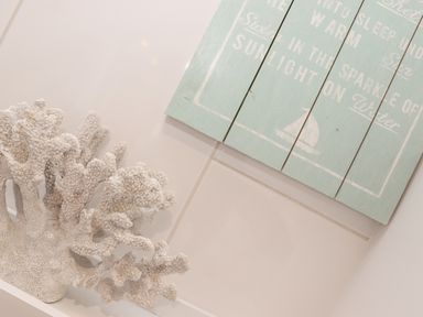 A white coral decoration next to a blue wooden wall sign with white text and a sailboat image at Kober House in Mullion