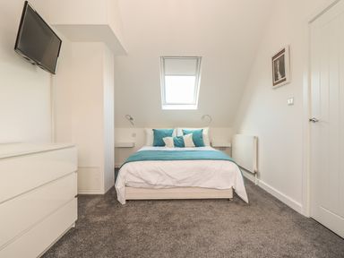 A bedroom with a bed blue and white bedding a chest of drawers a wall-mounted television a window and a door at Kober House in Mullion