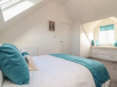 A bedroom with a bed with teal and white bedding a window seat with cushions and drawers in Kober House Mullion