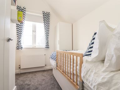 A bedroom with a single bed with wooden safety rail blue and white curtains and a white wardrobe at Kober House in Mullion