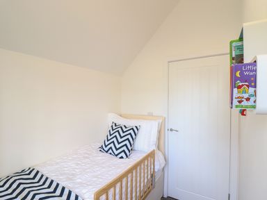 A small bedroom with a single bed pillow and blanket with zigzag pattern and a door next to a white wall shelf holding books at Kober House in Mullion