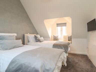 A bedroom with two single beds a window seat with cushions and a wall-mounted TV at Kober House in Mullion