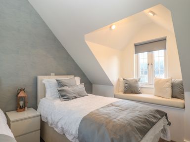 A bedroom with a single bed, bedside table, window seat with cushions at Kober House in Mullion