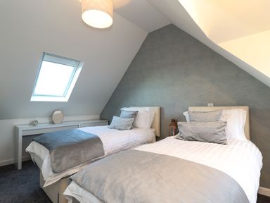 A bedroom with two single beds with gray and white bedding under a slanted ceiling with a skylight window at Kober House in Mullion