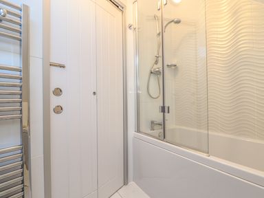 A bathroom with a bathtub and shower combination featuring glass doors and a wall with wave design at Kober House in Mullion