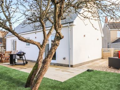 A backyard with a tree lawn chairs a barbecue and a white house at Kober House in Mullion