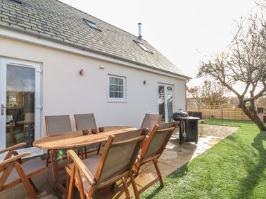 An outdoor patio with a wooden table and chairs next to a house with a gravel roof and a grassy yard at Kober House in Mullion