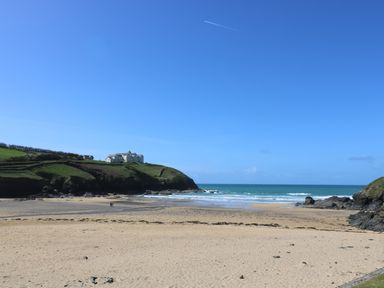 A sandy beach with rocks and waves under a clear sky near green hills with houses at Kober House in Mullion
