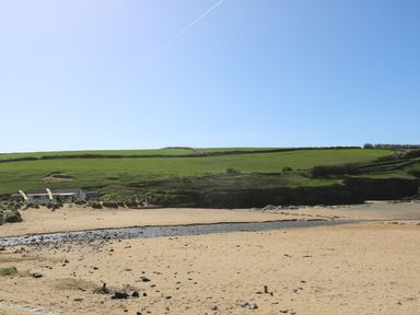 A sandy beach with rocks and a grassy hill beyond with a small building and flags at Kober House in Mullion