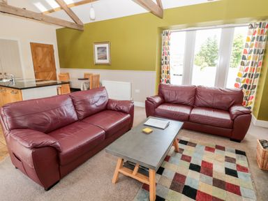 A living room with two red leather sofas a coffee table a multicolored rug and a dining table with chairs at Hemmel Cottage in Chatton