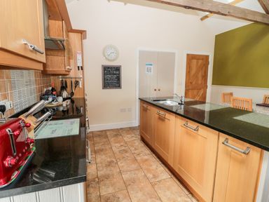 A kitchen with wooden cabinets black countertops a red toaster a stove a sink a dining table with chairs and tiled floor at Hemmel Cottage in Chatton