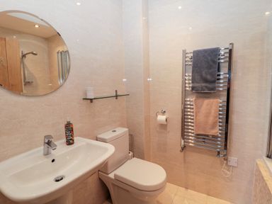 A bathroom with a sink toilet round mirror and towel rack at Hemmel Cottage in Chatton