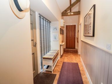 A hallway with a cushioned bench near window blinds and a wooden door at Hemmel Cottage in Chatton