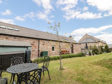A garden with outdoor table and chairs in front of a stone building at Hemmel Cottage in Chatton