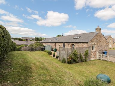 A stone cottage with a lawn and fence under a partly cloudy sky at Hemmel Cottage in Chatton