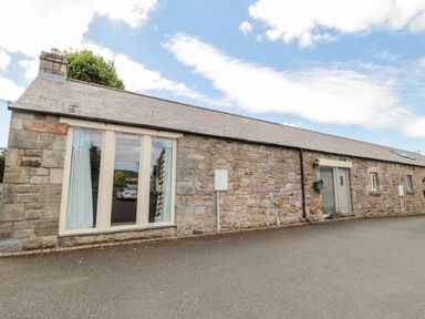 A stone cottage with large windows and a grey roof under a blue sky at Hemmel Cottage in Chatton