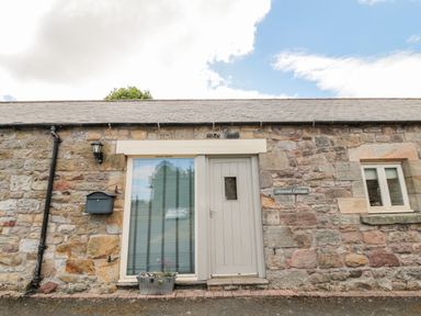 Stone exterior wall with a door and window with flowerpot and mailbox at Hemmel Cottage in Chatton