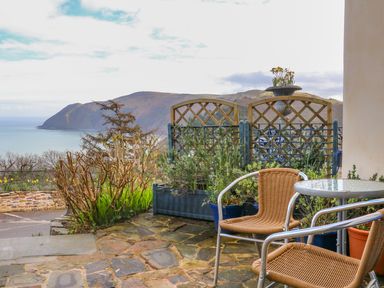 An outdoor patio with two wicker chairs and a small table overlooking a coastal mountain view at Bayview Terrace in Lynton