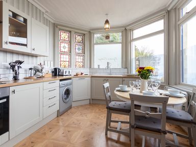 A kitchen with white cabinets wooden countertops a round dining table with chairs and flowers in a vase at Bayview Terrace in Lynton