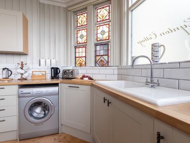 A kitchen with a washing machine toaster kettle and a sink under stained glass windows at Bayview Terrace in Lynton