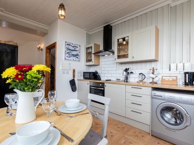 A kitchen with white cabinets a wooden countertop a washing machine and a dining table with flowers at Bayview Terrace in Lynton