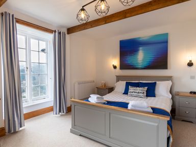 A bedroom with a bed with blue pillows and folded towels two nightstands and a window with striped curtains at Bayview Terrace in Lynton
