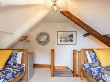 A bedroom with two single beds with floral bedding yellow pillows a circular mirror a framed picture and wooden ceiling beams at Bayview Terrace in Lynton