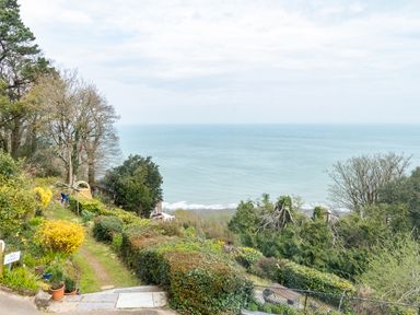 A coastal garden with shrubs, trees, a path, and a view of the sea at Bayview Terrace in Lynton