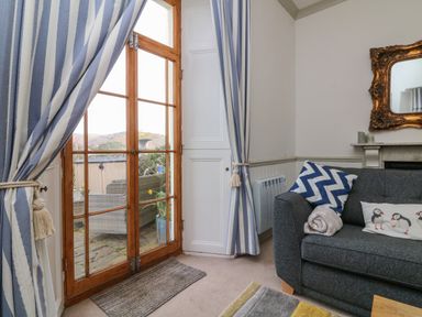 A living room with a gray sofa and patterned cushions next to wooden framed glass doors with striped curtains at Bayview Terrace in Lynton