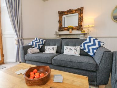 A living room with a gray sofa with patterned pillows and a wooden bowl with oranges on the coffee table at Bayview Terrace in Lynton