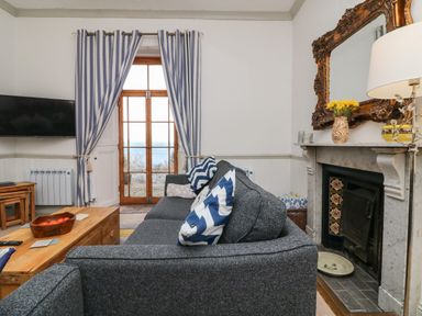 A living room with a gray sofa and chevron pillows a wooden coffee table a fireplace and striped curtains at Bayview Terrace in Lynton