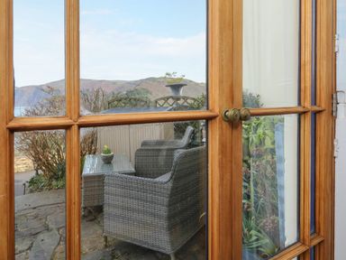 Wood framed glass doors opening to a patio with wicker chairs and a table with plants at Bayview Terrace in Lynton