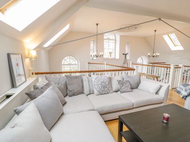 A living area with a gray sectional sofa and pillows and a black coffee table under skylights and chandeliers at Horeb Chapel House in Tanygrisiau