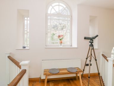 A hallway with a wooden bench, a telescope on a tripod, and flowers on the windowsill at Horeb Chapel House in Tanygrisiau