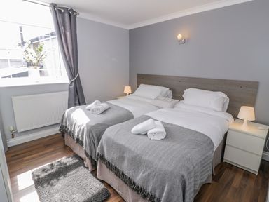 A bedroom with two single beds with gray blankets and white pillows a nightstand with a lamp and a gray curtain at Horeb Chapel House in Tanygrisiau