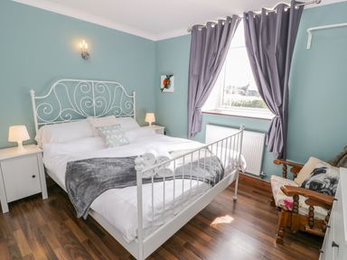 A bedroom with a white metal bed frame bedside tables lamps a wooden chair and curtains at Horeb Chapel House in Tanygrisiau