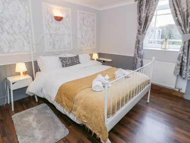 A bedroom with a white metal bed frame a yellow blanket bedside tables with lamps and a window with curtains at Horeb Chapel House in Tanygrisiau